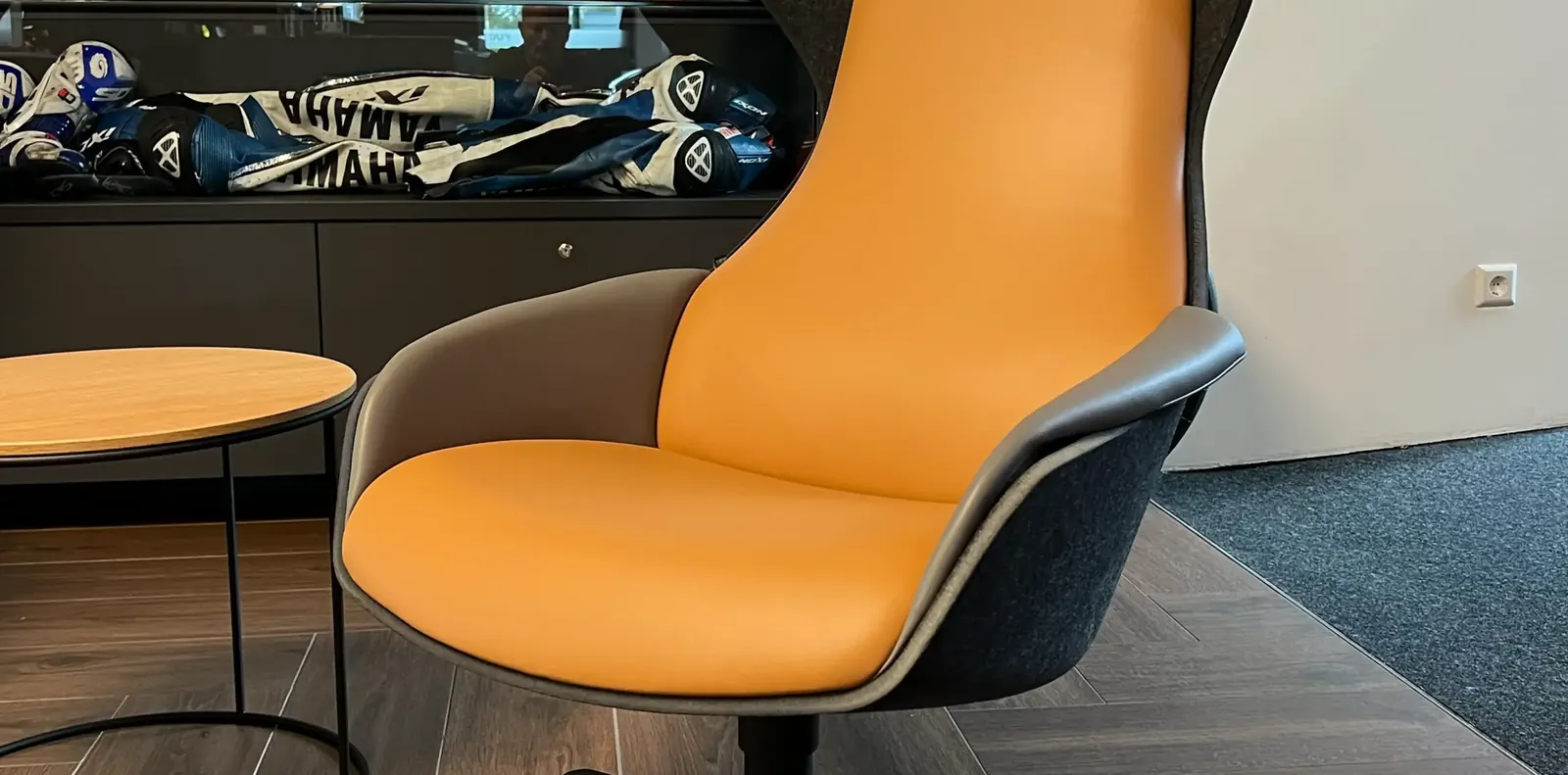 Detail eines Loungesessels mit orangefarbener Lederpolsterung und anthrazitfarbener Filzschale auf Fischgrätboden.