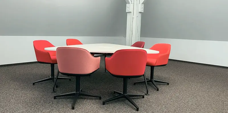 Besprechungsinsel mit weißer Tischplatte, umringt von roten und rosafarbenen Polsterschalenstühlen auf schwarzem Sternfuß.