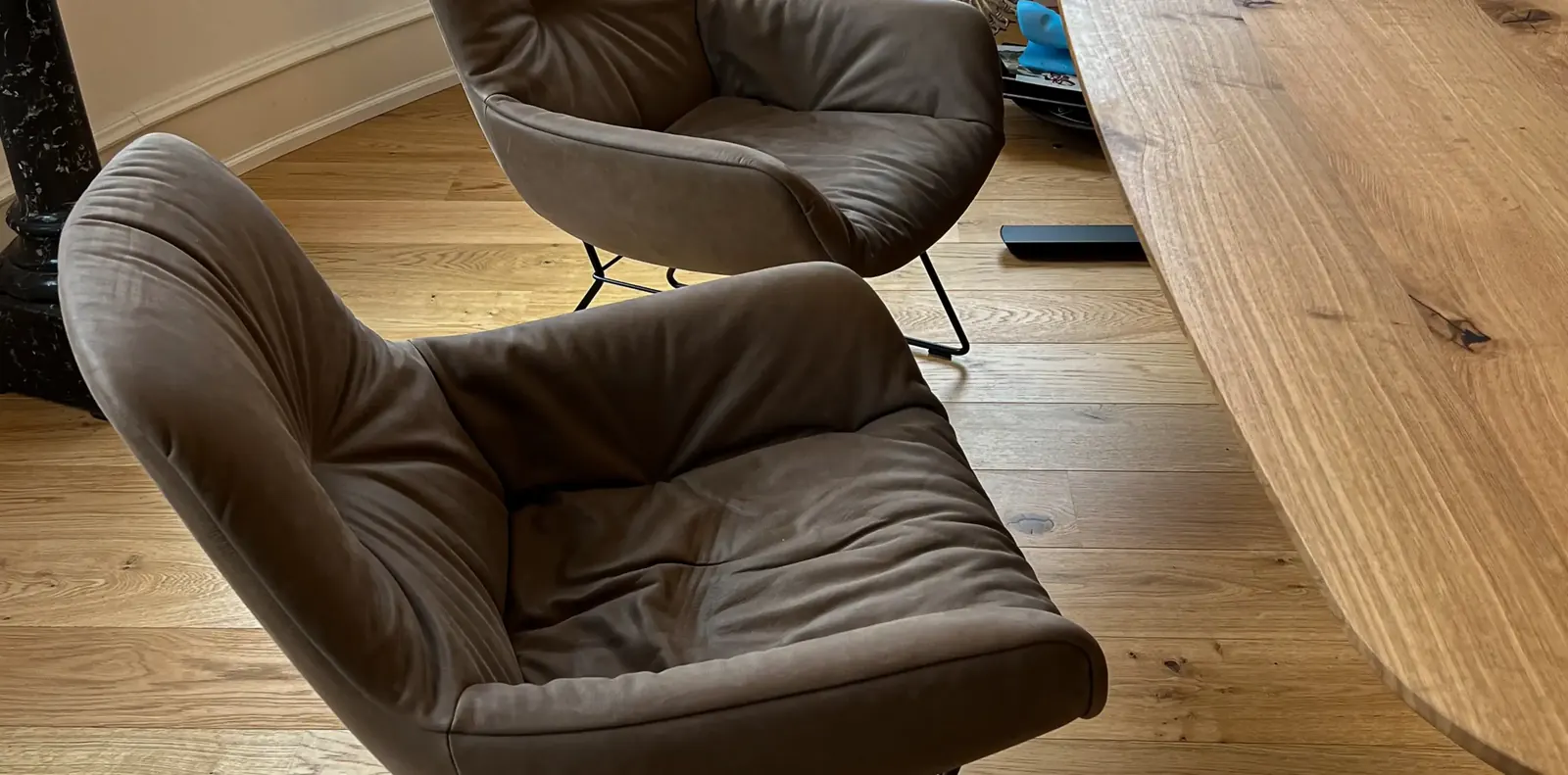 Blick von oben auf einen gepolsterten Freifrau-Sessel in Taupe neben einer massiven Holztischplatte mit Baumkante.
