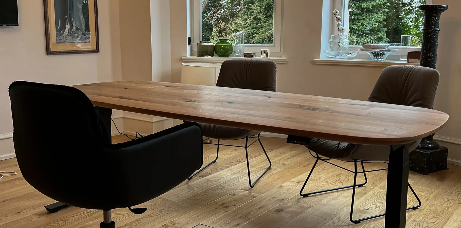 Esszimmer mit langem Holztisch, taupefarbenen Freifrau-Sesseln auf Drahtgestell und schwarzem Drehsessel am Kopfende.