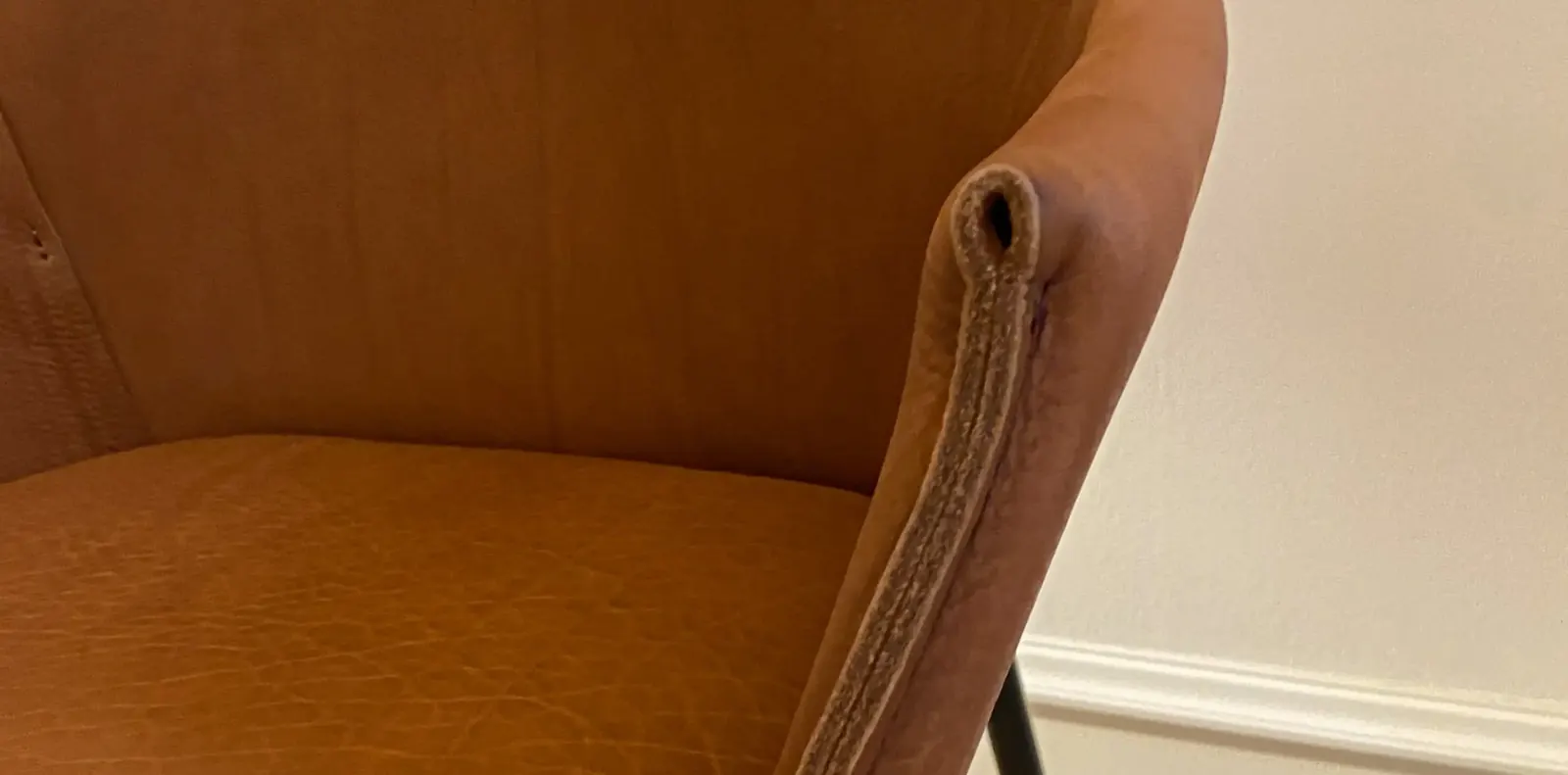 Nahaufnahme der cognacfarbenen Lederschale eines Armlehnstuhls mit sichtbarer Kantennaht.
