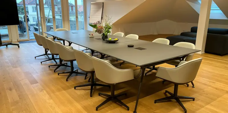Konferenzraum unter Dachschrägen mit langem anthrazitfarbenem Tisch, cremefarbenen Schalensesseln und Eichenparkett.