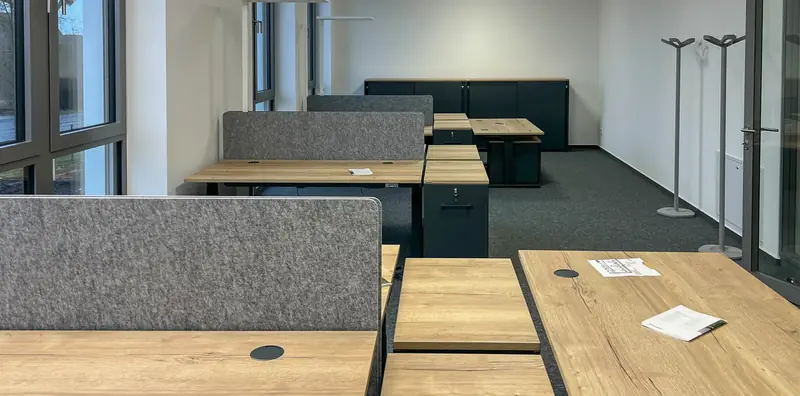 Großraumbüro mit Schreibtischen in Eichenoptik, grauen Filz-Trennwänden und anthrazitfarbenen Rollcontainern.