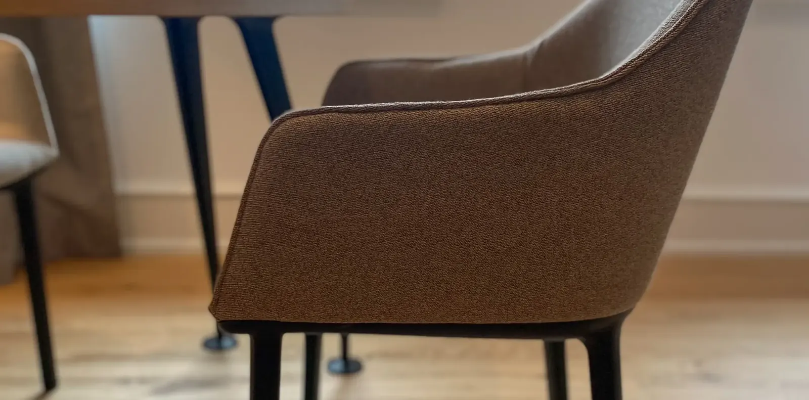 Detail eines Polsterstuhls mit braun meliertem Stoffbezug und schwarzen Beinen auf hellem Eichenboden.