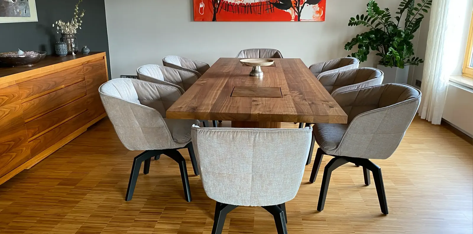 Essbereich mit massivem Nussbaumtisch, acht hellgrauen Polsterdrehstühlen auf schwarzem Fuß und einem Holzsideboard.